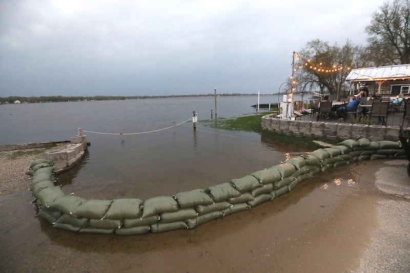 People hang out on the deck of the Bru Crew Bar and Grill as sandbags line the boat ramp area next to the restaurant on Friday, April 17, 2026, in Johnsburg.