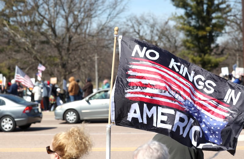 A flag waves in the wind as protesters and vehicles line Sycamore Road in DeKalb Saturday, March 28, 2026, during a No Kings march and rally against the federal actions of President Donald Trump and his administration.