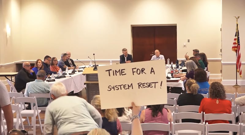 A Crystal Lake resident holds up a sign reading "Time for a system reset" during a Crystal Lake Park District board meeting on May 18, 2026.