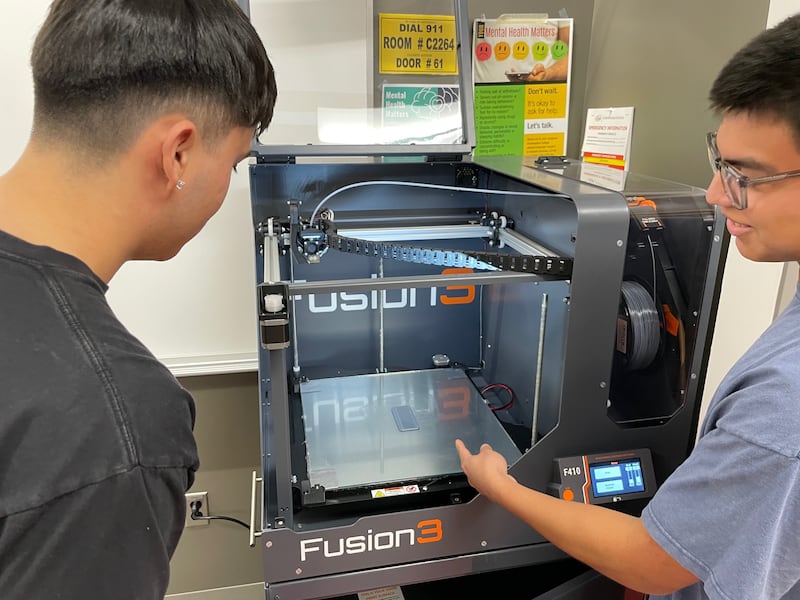 Jayson Quintero and Irving Escalante, participants in the Smitty Assistantship, utilize a Fusion3 3D printer in the physics/engineering lab.