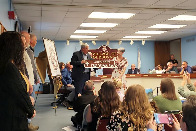 Bourbonnais Mayor Paul Schore is honored with a sign presented by Assistant Administrator Laurie Cyr, right, designating the street Schore lives on, Blanchette, as Honorary Paul Schore Avenue at the village board meeting on Monday, April 21, 2025.