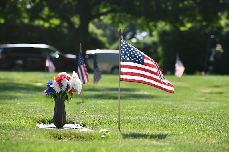 A flag billows in the wind next to a veteran's grave at Kankakee Memorial Gardens ahead of Memorial Day weekend in 2023. The annual tradition is completed by volunteers with the Kankakee County Veterans Council over the course of two days across three local cemeteries.