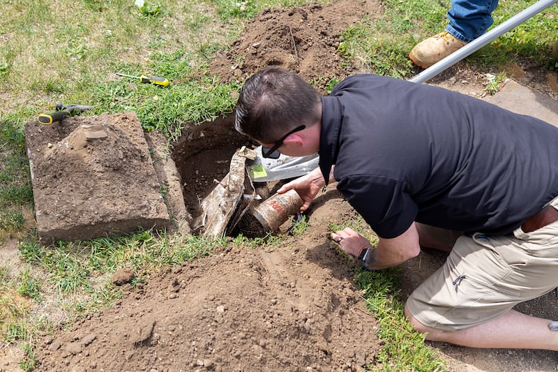 Jacinta Vazquez pulls out the first item, a DARE plastic cup, from the Thome School time capsule Sunday, May 31, 2026. Over the years the cooler collapsed and the inside filled with dirt and roots. Most of the paper items were ruined.