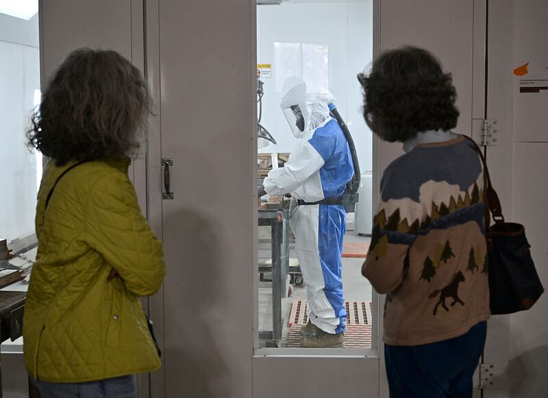 Visitors observe a Restoration Works Inc. worker using the company's patented Light Wave Stripper on window frames from Ellis Island.