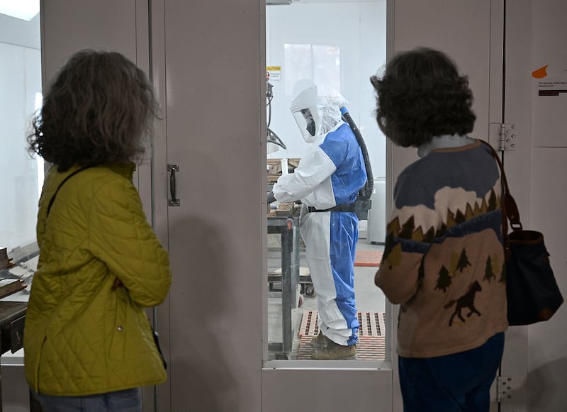 Visitors observe a Restoration Works Inc. worker using the company's patented Light Wave Stripper on window frames from Ellis Island.