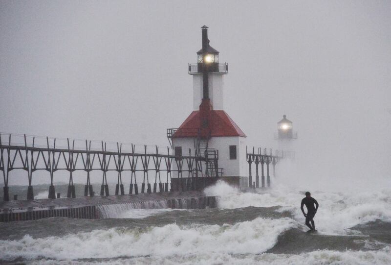 A surfer rides through blowing snow as Lake Michigan waves crash into the St. Joseph Inner and Outer Lighthouses Wednesday, Nov. 26, 2025, in St. Joseph, Mich. (Don Campbell/The Herald-Palladium via AP)