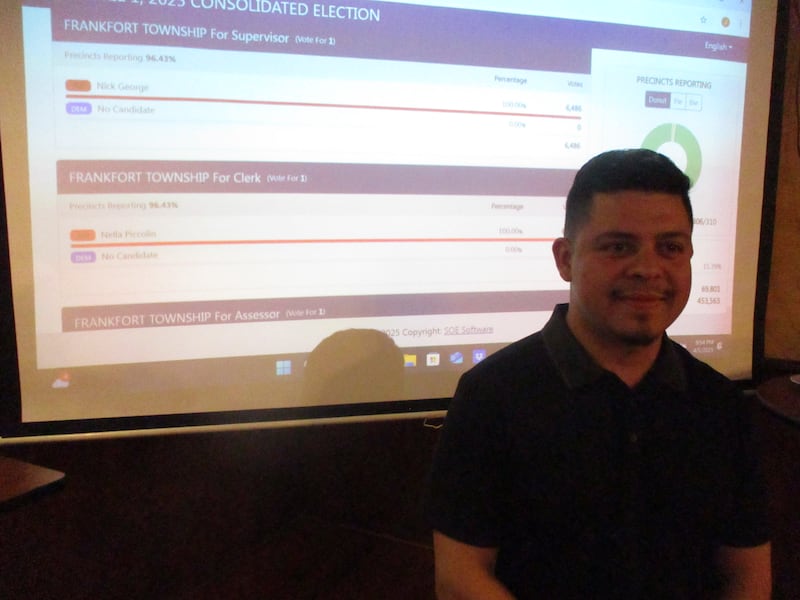Juan Moreno, stands in front of a screen showing Will County election results, at an election watch party on Tuesday night. April 1, 2025