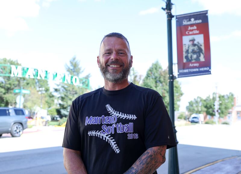 Josh Carlile, a Manteno teacher and softball coach and an Army veteran, stands near his Hometown Hero banner in downtown Manteno. His banner hangs nearby his fellow family members that also served.