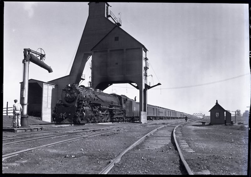 A steam-engine train is seen heading down a railroad track, passing a coal tower in DeKalb.