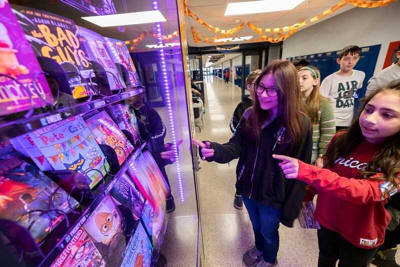 Students watch as a book choice falls from the rack Tuesday, March 25, 2025, in the book vending machine at Lincoln School in Sterling.