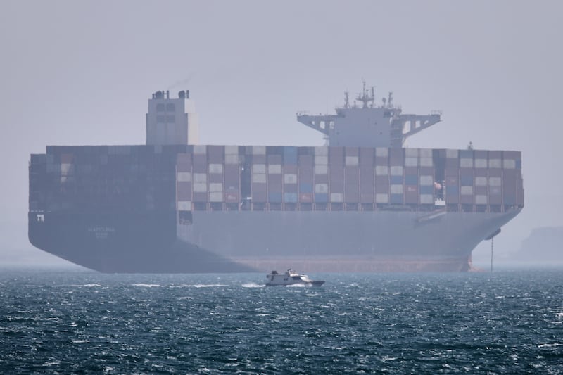 A container ship sits at anchor as a small motorboat passes in the foreground in the Strait of Hormuz off Bandar Abbas, Iran, Saturday, May 2, 2026. (Amirhosein Khorgooi/ISNA via AP)