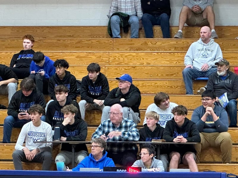 Members of Woodstock's boys basketball program sit with PA announcer Jack Darby  (plaid shirt) during a JV basketball game.