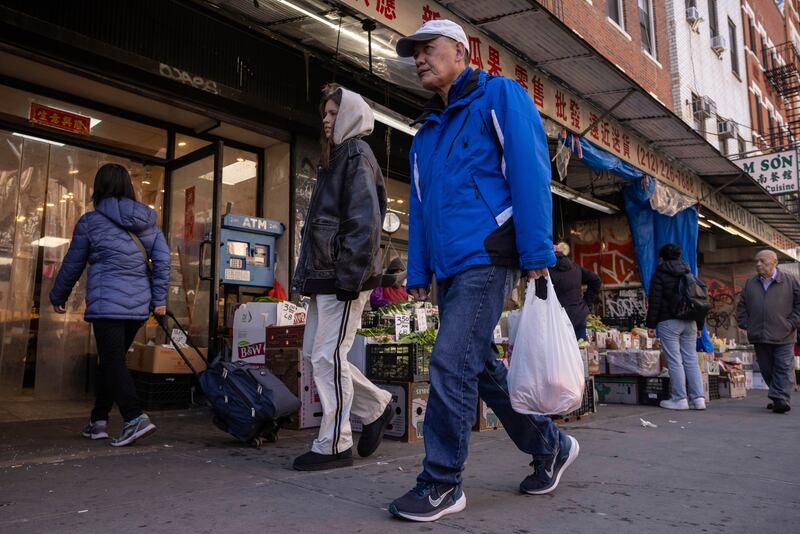 A person carrying a shopping bag walks past a grocery store in the Chinatown neighborhood, Wednesday, April 9, 2025, in New York. (AP Photo/Yuki Iwamura)