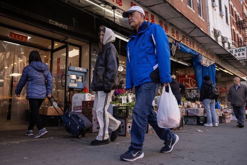A person carrying a shopping bag walks past a grocery store in the Chinatown neighborhood, Wednesday, April 9, 2025, in New York. (AP Photo/Yuki Iwamura)