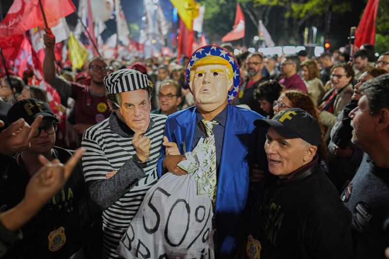 Protesters wearing masks of U.S. President Donald Trump and former President Jair Bolsonaro as a prisoner, protest Trump's announcement of 50% tariffs on Brazilian goods, in Sao Paulo, Thursday, July 10, 2025. (AP Photo/Andre Penner)