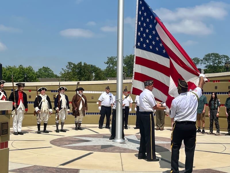Adorning Revolutionary War-style uniforms, the Sons of the American Revolution stand in attention as the American flag is raised to a trumpet call during Batavia's Flag Day ceremony.