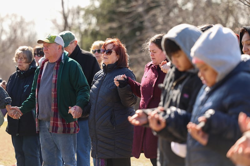 Kathy Dummer, center, and her husband Jeff, left, of Aroma Park, join hands with fellow parishioners and residents as they participate in a Mass and prayer service held in Aroma Park on Thursday, March 12, 2026, following the EF-3 tornado that tore through the town and Kankakee County on March 10.