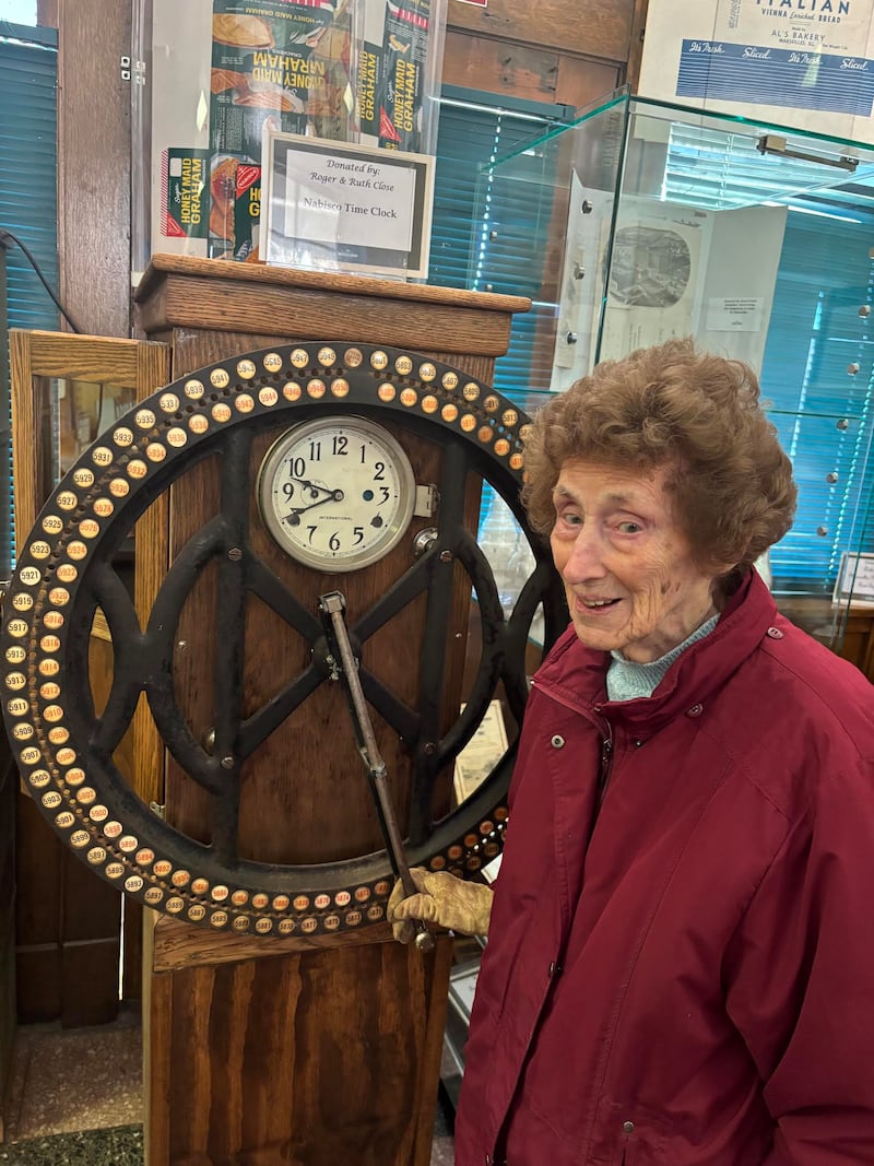 Showing the display and explaining how Nabisco employees moved the time clock wheel to punch their unique number, is Doris Sobinsky, a museum volunteer. Sobrinsky, who is 98 years old, was employed as a clerk at Nabisco and still knows how to use the time-clock.