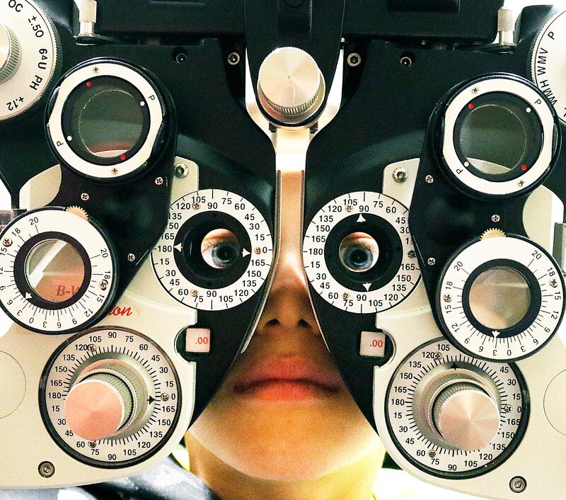 A patient peers through a refractor during an examination.