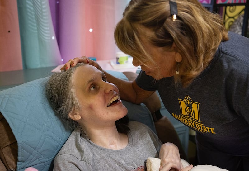 Cortnie Stewart, who suffered a traumatic brain injury in a 1997 car crash, looks up at her mother Judy Stegle at their home in Jonesboro, Illinois. A nearby nonprofit provided respite services to aid in her full-time care before closing as result of the budget impasse.