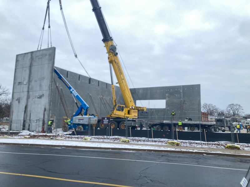 A crane install a wall of Gompers Jr. High's new gym while workers brace it in place.