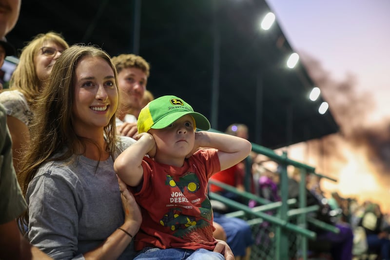 Donning his John Deere hat and t-shirt, three-year-old Quin Ketelaar, of Dyer, Ind., is held by his aunt, Emma Smits, of Beecher, as he covers his ears while a tractor competes in the Illinois Tractor Pulling Association Truck and Tractor Pull at the Will County Fair on Aug. 21, 2025.