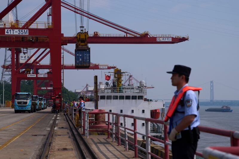 Policemen stand watch while cranes load containers onto trucks at the Yangluo Port in Wuhan, central China's Hubei Province, Friday, May 23, 2025. (AP Photo/Andy Wong)