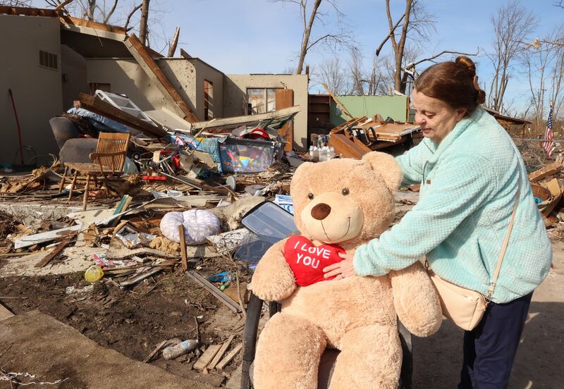 Aroma Park resident Patricia Kime adjusts a giant teddy bear in her driveway on March 12, 2026, in front of her home on Strasma NorthDrive, which was destroyed by the March 10 EF-3 tornado. She pulled the teddy bear from her former living room in hopes to put a smile on her neighbors' faces, she said. The bathroom she was sheltering in was the only intact room of her home.