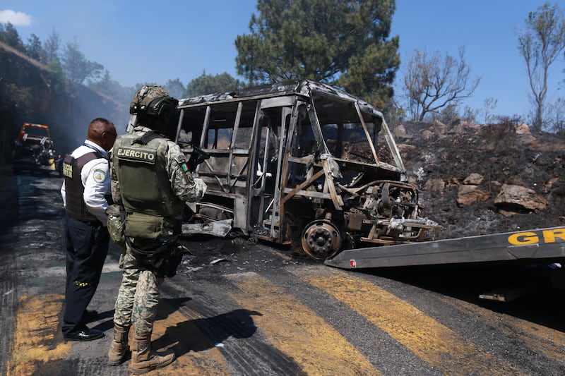 A soldier stands guard by a charred vehicle that was set on fire in Cointzio, Mexico, Sunday, Feb. 22, 2026, amid reports the Mexican Army killed Jalisco New Generation Cartel leader Nemesio Oseguera, known as "El Mencho." (AP Photo/Armando Solis)