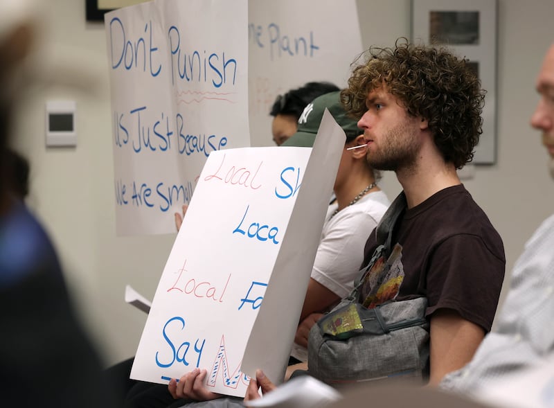 Audience members hold signs Monday, June 23, 2025, opposed to amending the city code to prohibit the sale of illicit THC products and kratom within DeKalb during the city council meeting at the DeKalb Public Library.