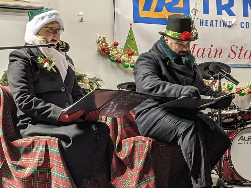 Oswego village trustees Karen Novy, left, and Andrew Torres, right, read the poem “Twas the Night Before Christmas” to those gathered in front of the main stage at the Oswego Christmas Walk on Dec. 6.