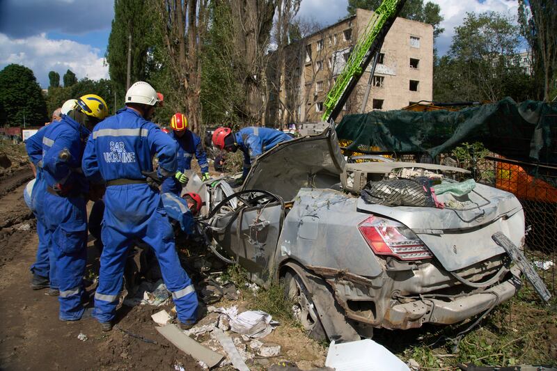 Emergency workers inspect a damaged car close to the multi-storey residential house that was ruined by a Russian missile Thursday night, killing 31 civilians including five children, in Kyiv, Ukraine, Friday, Aug. 1, 2025. (AP Photo/Efrem Lukatsky)