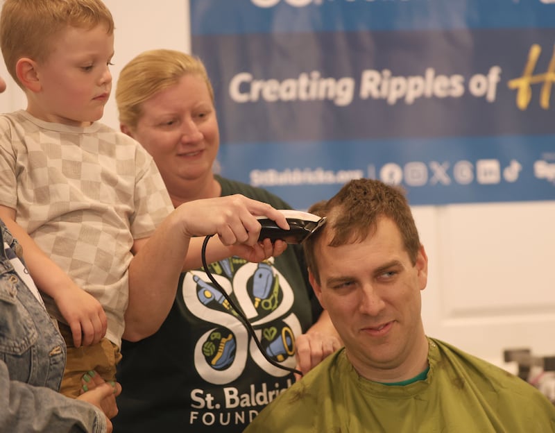 Evan Brown takes the first swipe of hair off of his dad, Utica Fire Chief Ben Brown, with the help of beautician Sarah Stewart, of Downstairs on 1st Day Spa, during the 19th annual Illinois Valley Emergency Services Annual St. Baldrick's Event on Sunday, March 22, 2026 at Senica's Oak Ridge in La Salle.