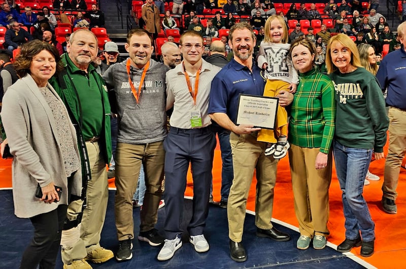 Mike Kimberlin (navy blue), a 2001 Bishop McNamara graduate, poses with his family after learning of his induction into the Illinois Wrestling Coaches and Officials Association Hall of Fame at the IHSA Boys Wrestling Individual State Finals at the State Farm Center in Champaign Saturday, 22, 2025.