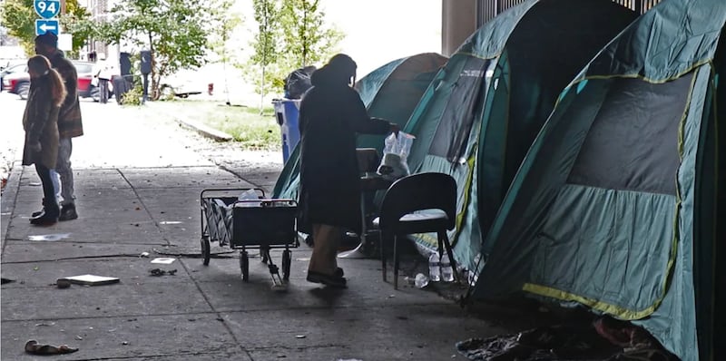 A volunteer with Street Samaritans hands out a care package to a person camping underneath a bridge in November in the Chicago area.