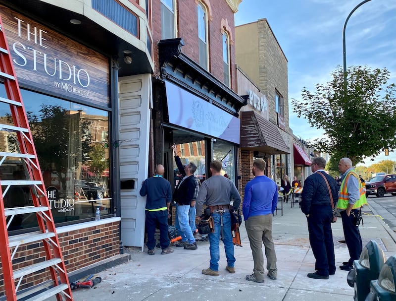 Sycamore city building inspectors, firefighters and police, including Fire Chief Bart Gilmore (second from right) watch as authorities review damage caused to the front of Atlas Roots Collective women's clothing store at 330 W. State St. in downtown Sycamore on Friday, Oct. 24, 2025. Police said a vehicle crashed into the front of the store, injuring a driver and a passenger.