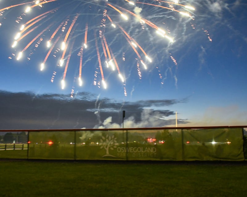 An Oswego Park District banner hangs on a baseball outfield fence at Prairie Point Community Park in Oswego as the fireworks display goes off on Thursday July 4, 2024.