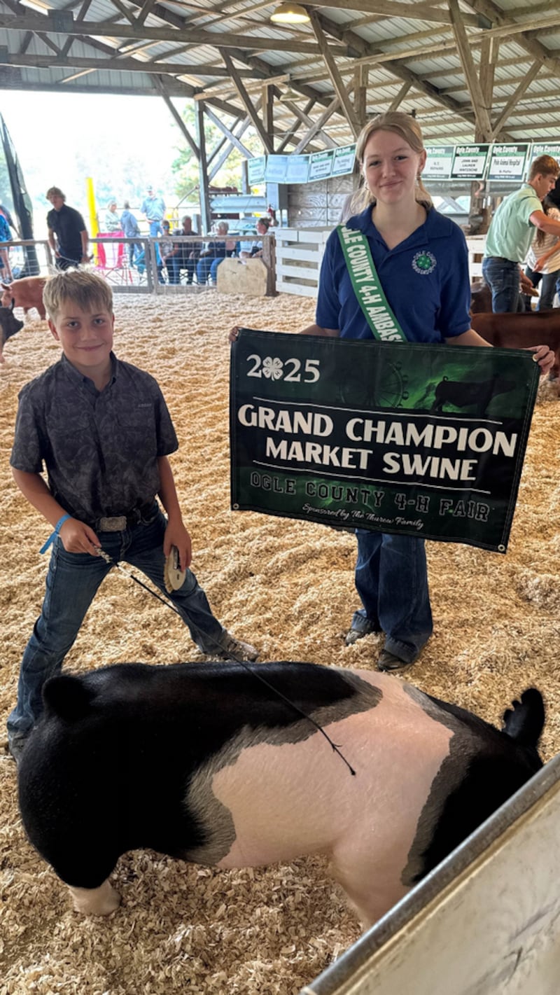 Jaxon Alderks (left) smiles after receiving the Grand Champion Market Swine banner from 4-H Ambassador Allissa Martin (right) during the 4-H Swine Show.
