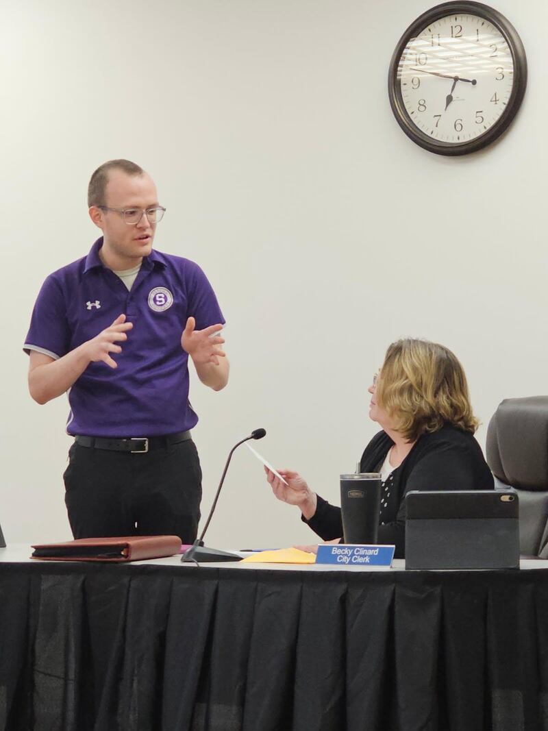 Oglesby City Clerk Becky Clinard (seated) is officially retired. Monday, Aug. 18, 2025, Clinard accepted parting gifts from the council via Commissioner Austin Cullinan (standing) and then challenged the council to be less contentious. “Will you forever be known as the council that can’t get along?” Clinard isn’t leaving city government altogether, as she was appointed Monday to the Zoning Board of Appeals. Mayor Jason Curran anticipated a Sept. 2 vote to install Clinard’s replacement.