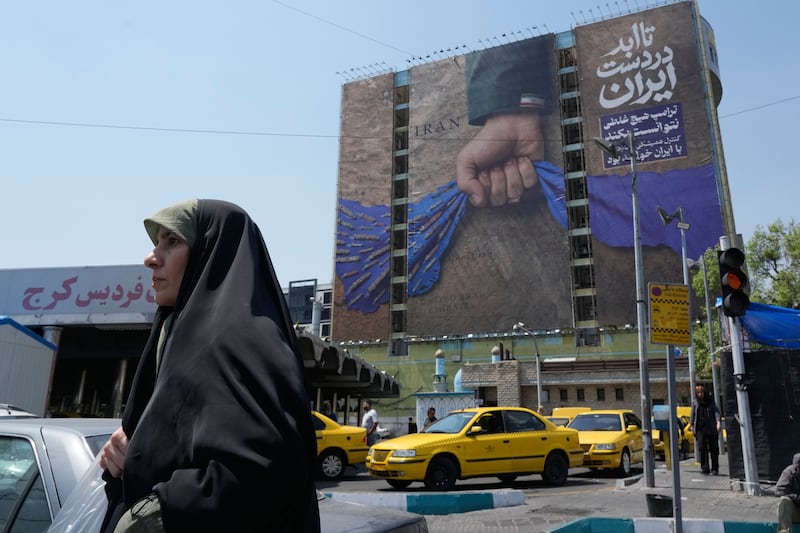 A woman walks past a billboard that shows a graphic depicting a military personnel's hand holding the Strait of Hormuz in his fist with signs which read in Farsi: "In Iran's hands forever," "Trump couldn't do a damn thing," " The control of Strait of Hormuz will be Iran's forever," in Vanak Square, in northern Tehran, Iran, Thursday, April 16, 2026. (AP Photo/Vahid Salemi)