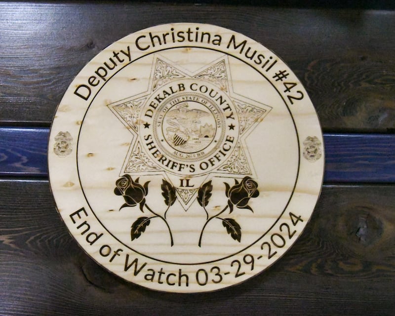 An engraved wood plaque is displayed on a table during a memorial vigil on Saturday, March 29, 2025, to mark one year since the late DeKalb County sheriff's deputy Christina Musil, 35, was killed in the line of duty in a rear-end car crash in Waterman while on patrol on March 28, 2024. The vigil was held at Sycamore High School's field house.