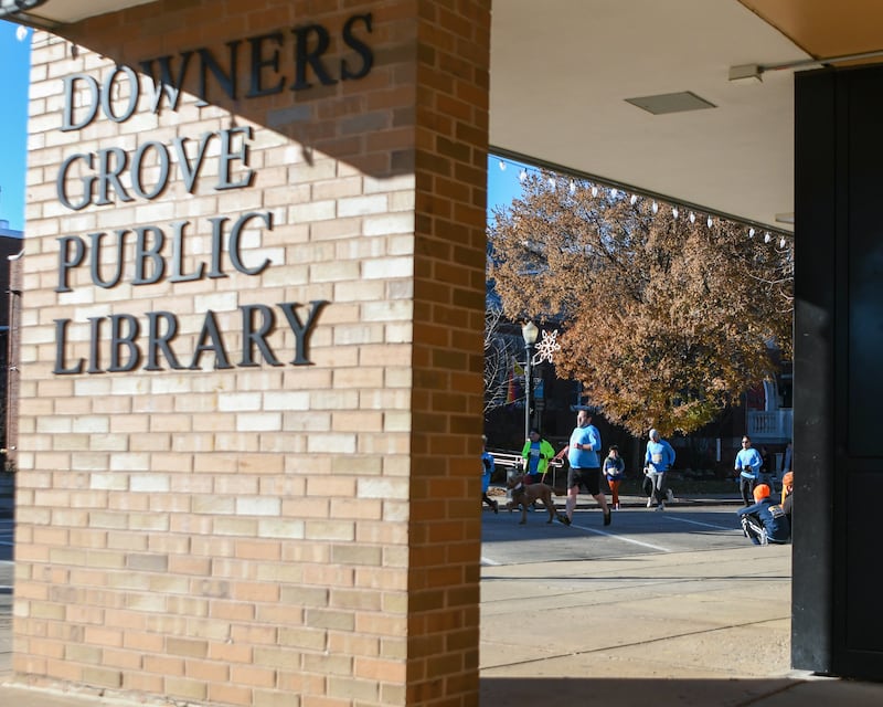Participants run past the Downers Grove Public library during the Grove Express 5k race in downtown Downers Grove on Thursday Nov. 23, 2023.