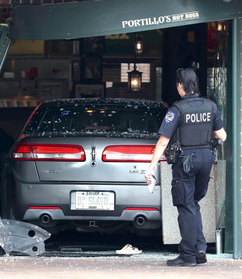 An Oswego Police officer surveys the scene Wednesday, July 30, 2025, where a car crashed through the front entrance of the Portillo’s at 2810 U.S. Route 34 in Oswego injuring 12.