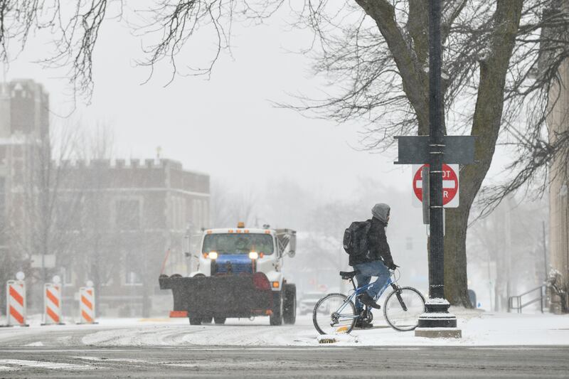 A snowplow travels along South Indiana Avenue as a bicyclist braves the wind Tuesday, Feb. 12, as snow arrived to the Kankakee area.