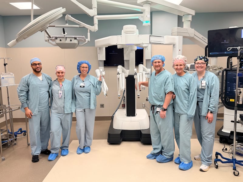 Members of the Morris Hospital surgical team with the component of the da Vinci 5 robotic-assisted surgical system that holds the camera and surgical instruments controlled by the surgeon from a console.