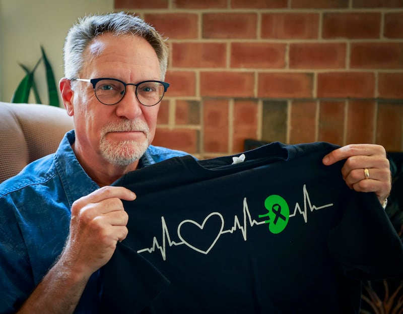 Mike Torti holds a kidney donor shirt Tuesday, June 10, 2025 at his house in Woodridge that his friends gave him. Torti donated his kidney via what is called a paired exchange to Jacob Fill, now 28, the son of a former Elmhurst neighbor who he hadn't seen in more than 20 years. Although Mike was a match, Fill's doctors determined that a younger donor would be preferable. Mike agreed to a paired donation where he donated a kidney to someone else so that Jacob could receive a kidney from a younger donor.