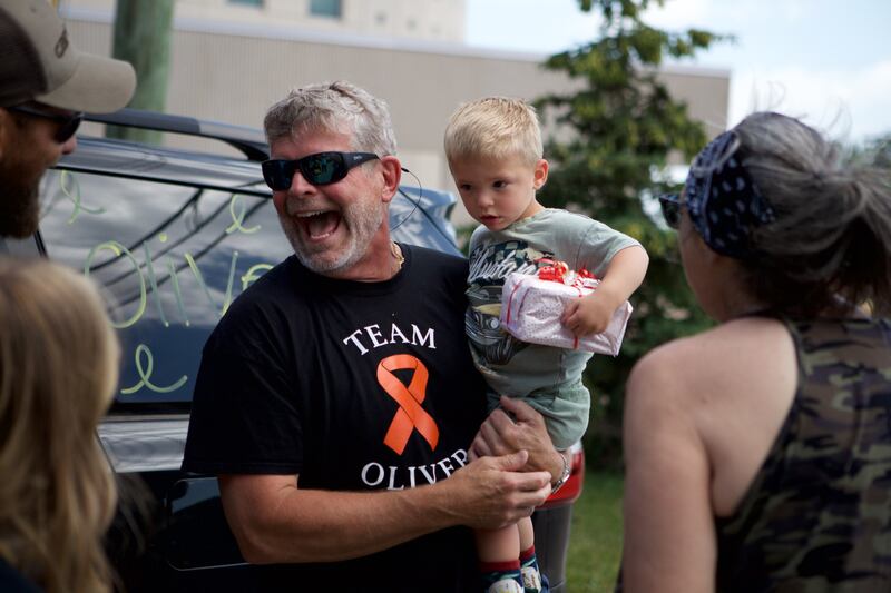 Oilver Olinger, 2, of Sycamore, held by Grandfather Keith Olinger receives a gift from motorcycle riders outside Sycamore Public Library on Sunday, June 22, 2025. Oliver was escorted by law enforcement and bikers to the St. Charles Motorcycle Museum to celebrate his cancer remission.