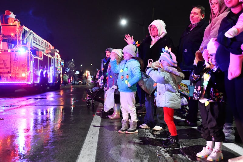 Children and attendees wave as firetrucks pass by on West Broadway Street during the 2023 Bradley Christmas Parade.