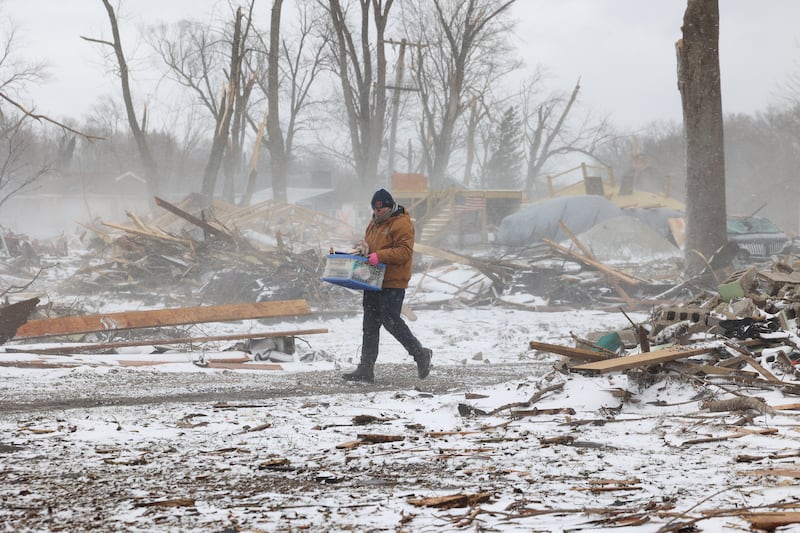 Near the summer home of Evanston residents Douglas Weber and Martha Plaza-Weber along South Sandbar Road in Aroma Township, their son-in-law Waldek Ziolkowski carries salvaged belongings from their demolished home a snow falls on March 16, 2026, following the March 10 tornado in Kankakee County.