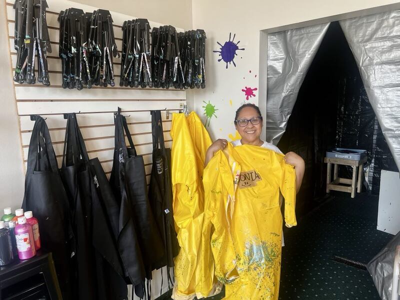 Sonia Robinson holds a paint poncho next to the splatter room inside her art studio, Color Me Happy, in Sterling, Illinois.